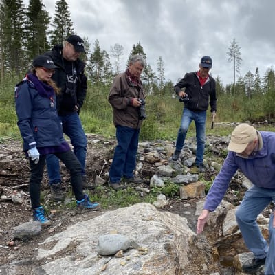 Fem personer står och tittar på en berggrund.