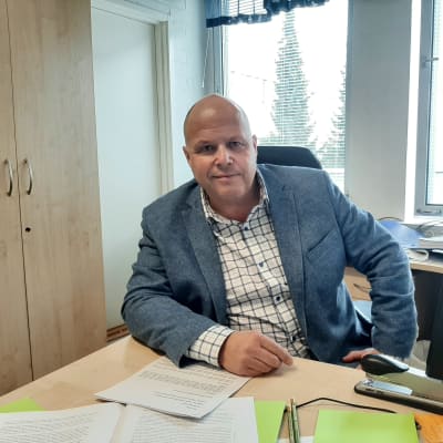 Man i blå kavaj sitter vid skrivbord.