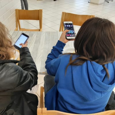 Två flickor sitter vid lunch med sina mobiltelefoner.