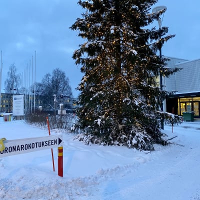 Joulukuusi, jonka taustalla Rovaniemen kaupungin rokotuspiste. Edustalla kyltti, jossa lukee Koronarokotukseen.