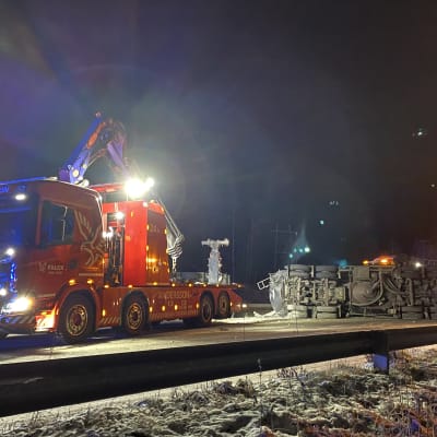 En bärgningsbil står framför en lastbil som har vält på vägen