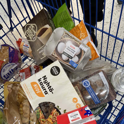 Ostoskärryt, missä on muunmuasa maitopurkki, leipää, munia ja nyhtökaurapakkaus