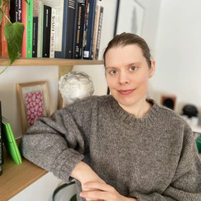 En mörkhårig kvinna framför en bokhylla.