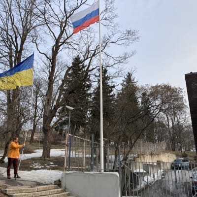 Mikko Kiiskinen kannattelee lipputankoa ja Venäjän pääkonsulaatin aidan vieressä. Hänen vieressään on konsulaatin lipputanko ja Venäjän lippu.