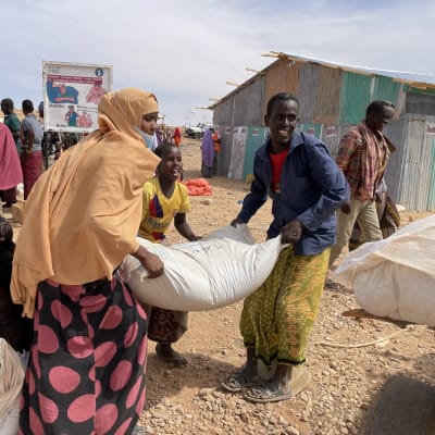 Nainen, lapsi ja mies nostavat avustusviljasäkkiä Adadlen alueella Somaliassa. 