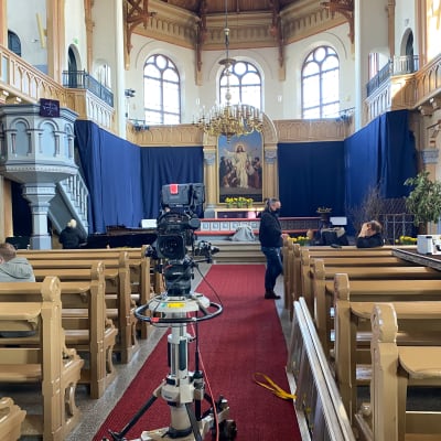 Bild mot altaret i en kyrka. Flera personer och flera filmkameror syns.
