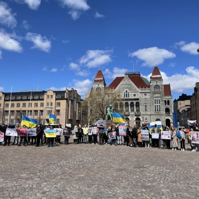 Demonstration på Järnvägstorget i Helsingfors, med plakat och ukrainska flaggor.