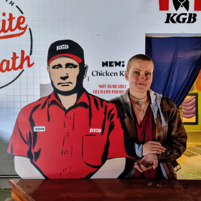 En kvinna står bredvid en figur föreställande Vladimir Putin som kassör i en snabbmatsrestaurang.