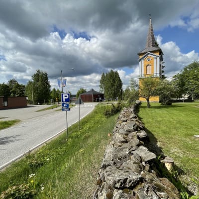 Kiihtelysvaaran keltainen kellotapuli ja etualalla kirkon vanhaa kiviaitaa.