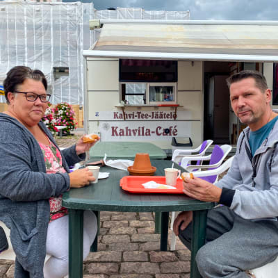 En kvinna och en man sitter vid ett bord på Lovisa torg. De har varsin munk i handen.
