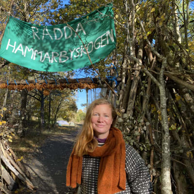 Sofia Olsson framför banderoll med texten rädda Hammarbyskogen