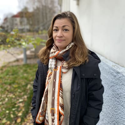 Amanda Löfman utomhus på hösten mot en ljusblå vägg. 