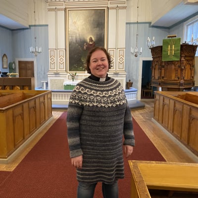 Kvinna med prästkrage framför altaret i en träkyrka.