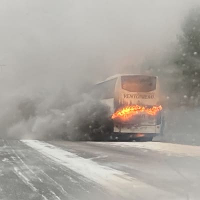 En buss brinner på vägkanten, snöfall på motorvägen. 