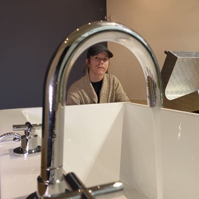 Eetu Huhtala sitter bredvid sitt verk där det rinner vatten ner i ett badkar. I bakgrunden syns ett annat verk som påminner om en ihopvikt fåtölj i kantig metall.
