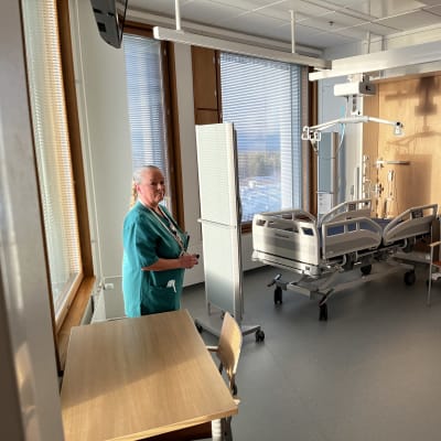 Ett tomt sjukhusrum med en kvinnlig sjukskötare i förgrunden. 