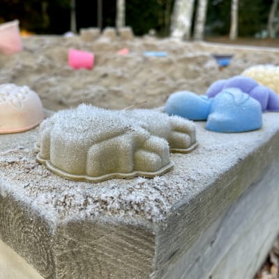 Blå, röda, gula och violetta formar för sandkakor på en sandlådskant. Motivet är täckt av rimfrost.