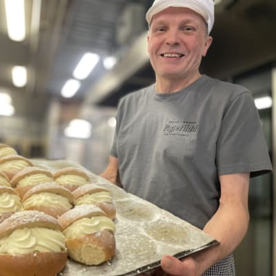 En glad man med vit skyddsmössa håller i en plåt med fastlagsbullar 