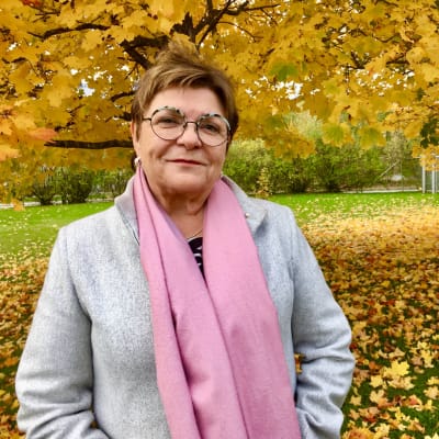 Porträtt på Maria Tolppanen. Hon står utomhus, ler, i bakgrunden träd i höstskrud.