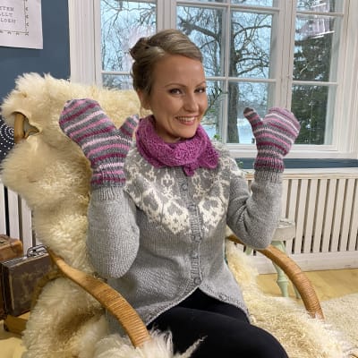 Kvinna sitter i en korgstol och har vantar på händerna som hon visar upp
