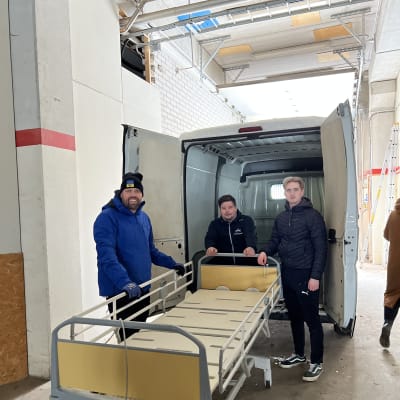 Tre män med en sjukhussäng utanför en skåpbil.