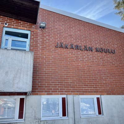 Jäkärlän koulun punatiilinen seinä. Seinässä lukee mustilla kirjaimilla "Jäkärlän koulu"