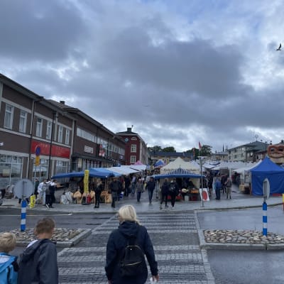 Marknad med torgförsäljning i Kristinestad. Människor rör sig i centrum av staden, det är regnvått.