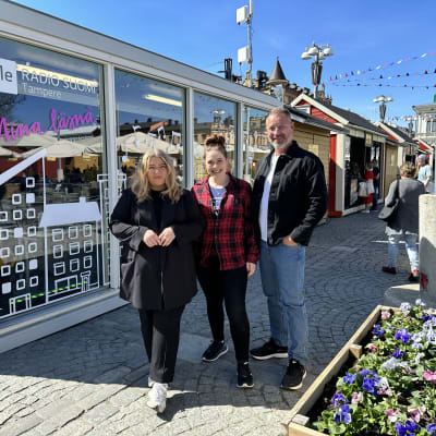 Radio Suomen toimittajat Miia Roivainen, Pauliina Puurila ja Mikko Hirvonen poseeraavat väliaikaisen lähetyskontin edessä.