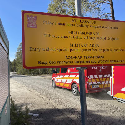 En skylt som informerar om att det är förbjudet att röra sig på militärområdet utan tillstånd. I bakgrunden räddningsverkets fordon. 