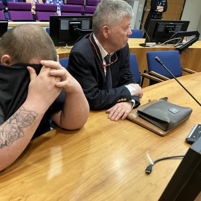 En tatuerad man täcker sitt ansikte.
