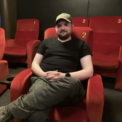 Mies istuu elokuvateatterin punaisella penkillä.