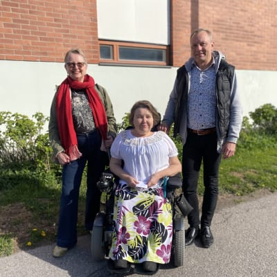 Två kvinnor och en man poserar framför husvägg