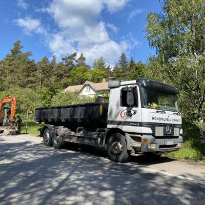 En grävmaskin och lastbil vid en vägren.