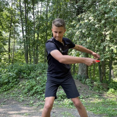 Nuori mies heittää frisbeegolfkiekkoa vehreässä metsikössä.
