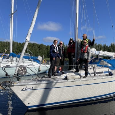 Viisi henkilöä lähdössä purjehtimaan noin 9 metriä pitkällä Aura-purjevenellä Joensuun Linnunlahden satamalaguunista.