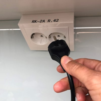 A hand putting a plug into a wall socket.