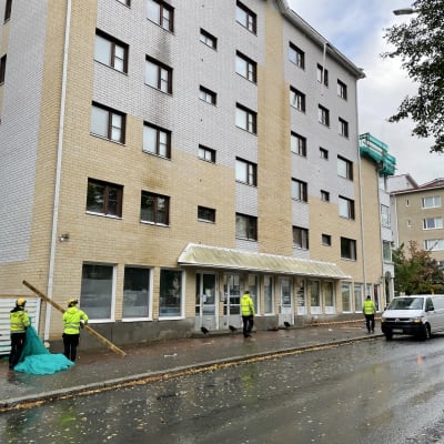 Huomioväreihin pukeutuneita henkilöitä keräämässä myrskytuhoja pois kerrostalon edustalta.