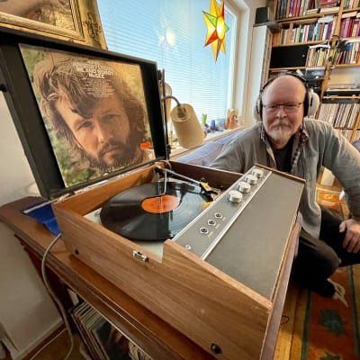 Äldre man lyssnar på vinylskiva hemma i sitt vardagsrum.