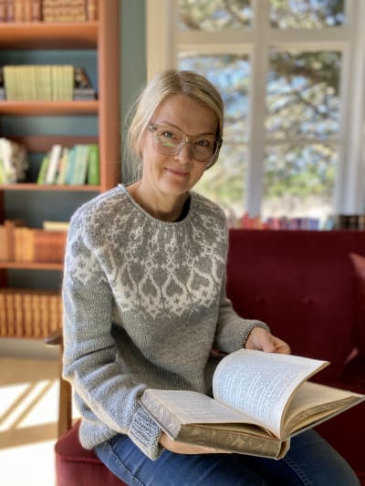 Anna Påfs-Streng sitter i Strömsös biliotek med en uppslagen bok i famnen.