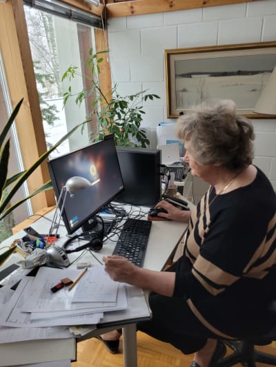 en äldre dam med grå lockar sitter vid sin dator