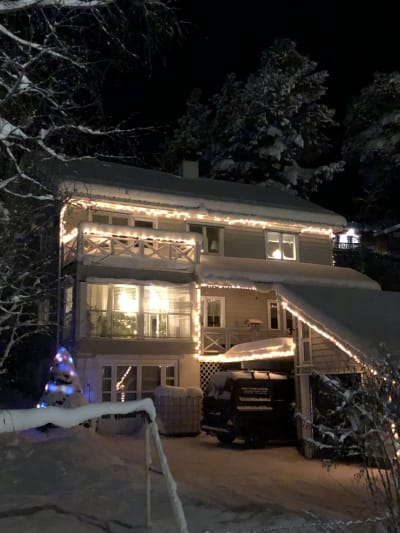 Ett hus i två våningar. Huset täckt av snö, det är kväll och lampor lyser inomhus. Huset är också pyntat med julbelysning.