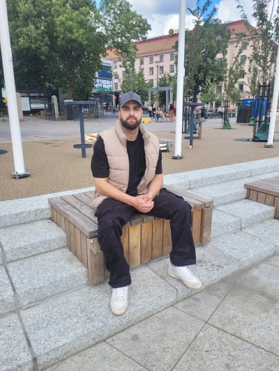 En man i keps och skägg sitter på en bänk på salutorget i Åbo. 