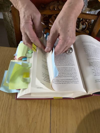 Händer som bläddrar i en bok med post-it-lappar.