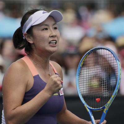 Peng Shuai pitää toista kättä nyrkissä ja toisessa kädessä tennismailaa.