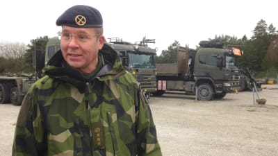 Mattias Ardin, leende, ser förbi kameran, militära lastbilar i bakgrunden.