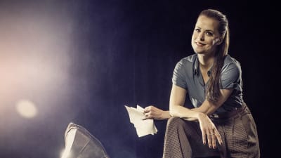 Skådespelaren Emma Klingenberg står på ett scengolv bredvid en grammofonspelare. På golvet ligger gamla papper kringströdda.