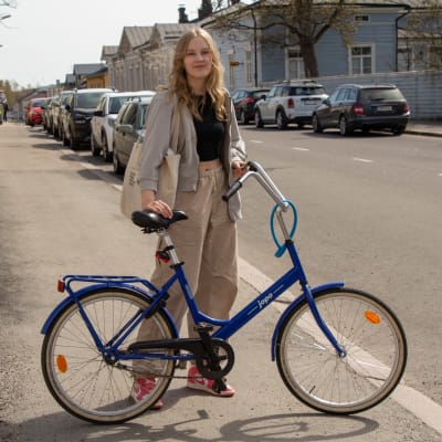 Ronja står på trottoaren med sin blåa cykel