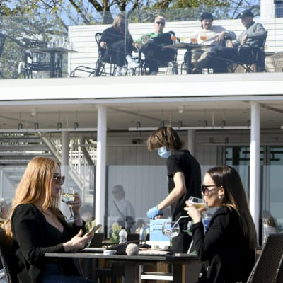 Asiakkaita Cafe Caruselin terassilla aurinkoisella säällä Helsingin Kaivopuistossa.