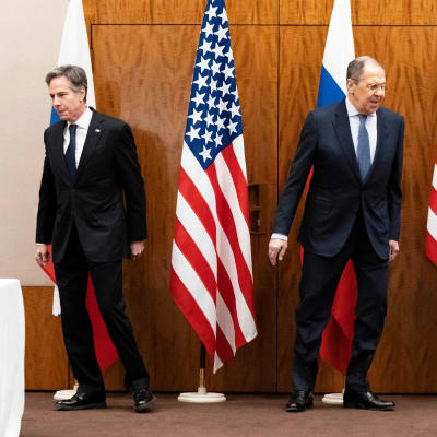 Antony Blinken och Sergei Lavrov på ett podium med amerikanska och ryska flaggor.
