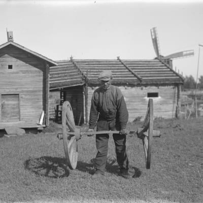 En man lyfter två kärrhjul. Bilden är tagen 1930 i Korsnäs.